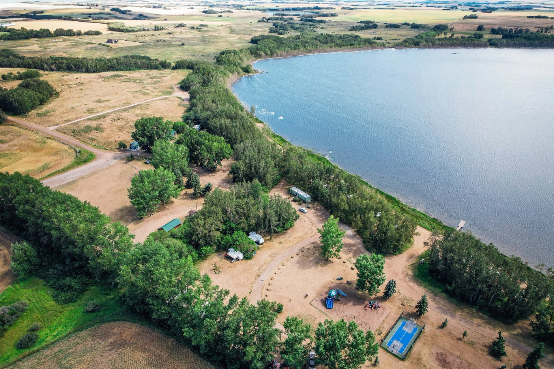Aerial view of a campground with trees, playground, sports courts, and a lake.