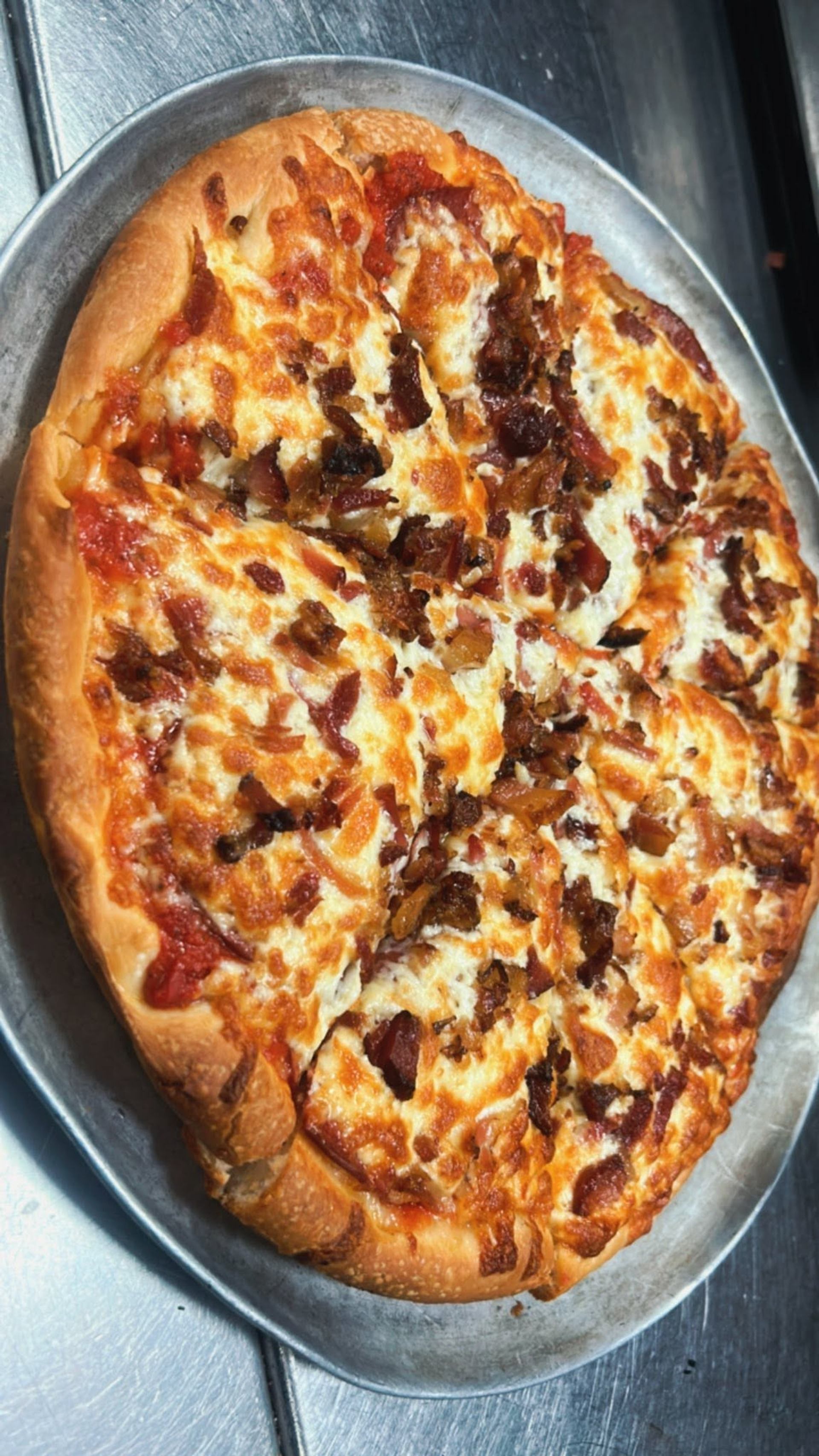 A baked pizza topped with cheese, bacon, and onions is sliced and served in a round pan.