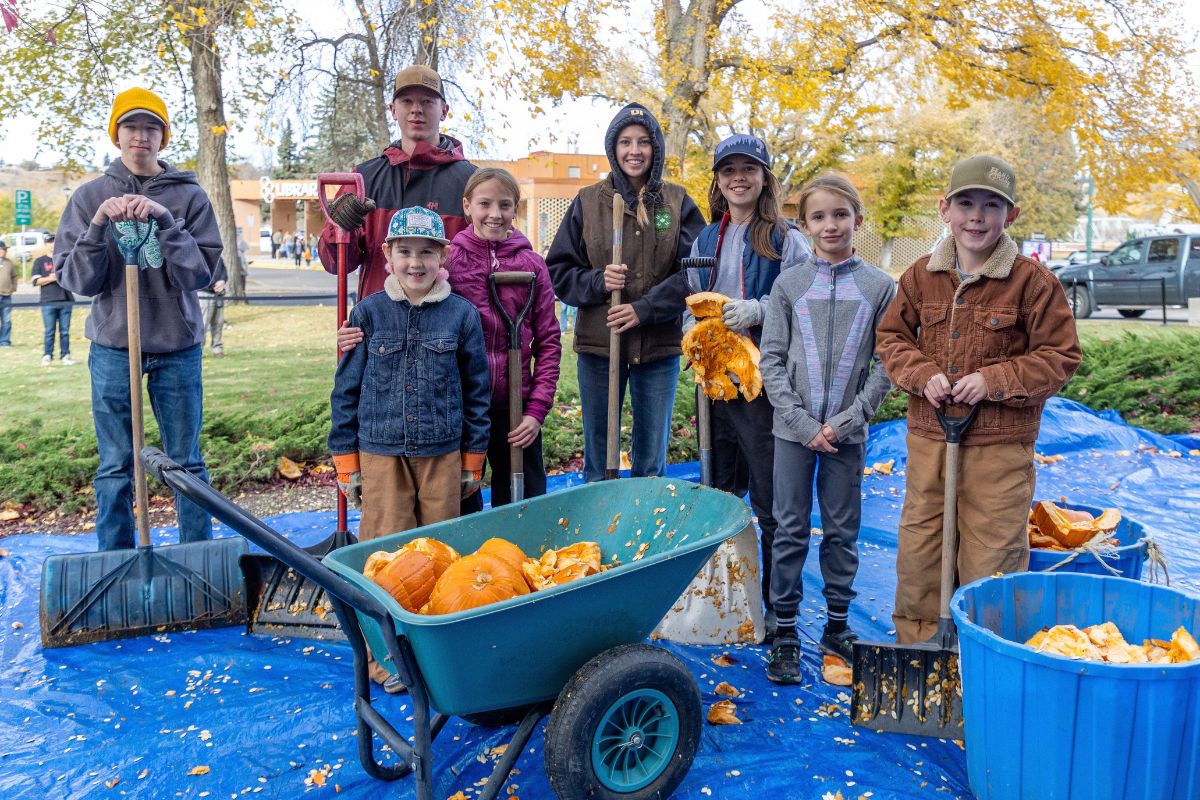 Group holding shovels beside a wheelbarrow and bins filled with smashed pumpkins.