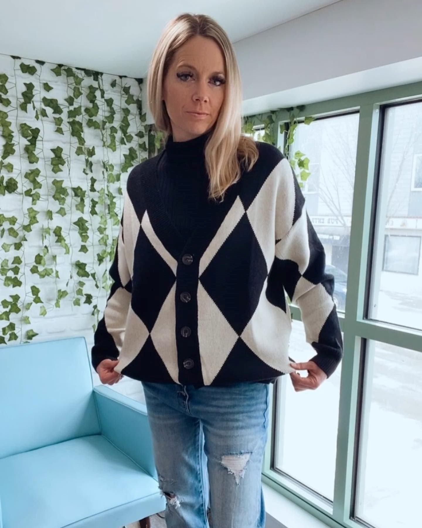 Retail clothing store interior with person standing wearing black-and-white argyle sweater and jeans.