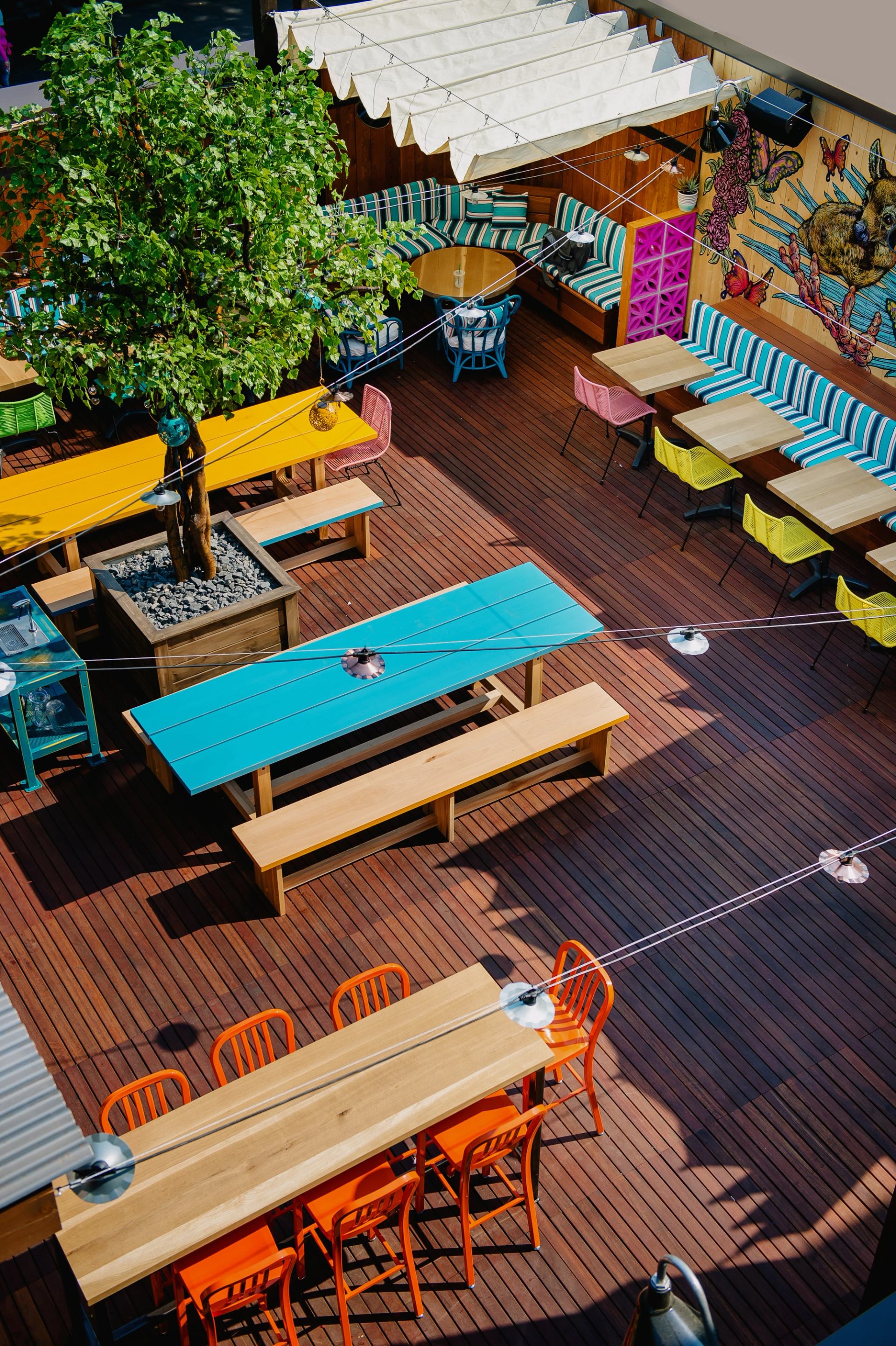 Vibrant outdoor patio with colorful tables, benches, and a mural on a wooden deck.