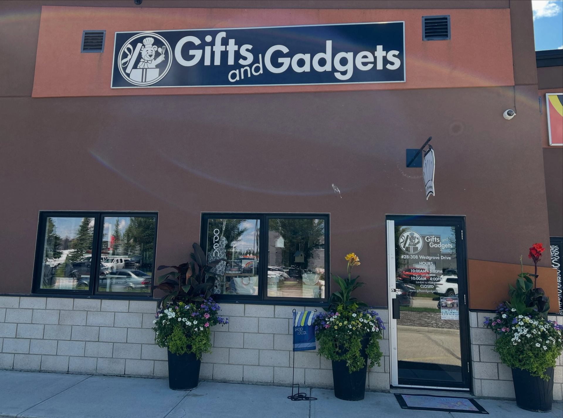 Storefront of Gifts and Gadgets with windows, glass door and large flower planters.