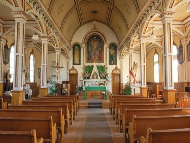 Interior of a church with wooden pews, altar, and arched windows.