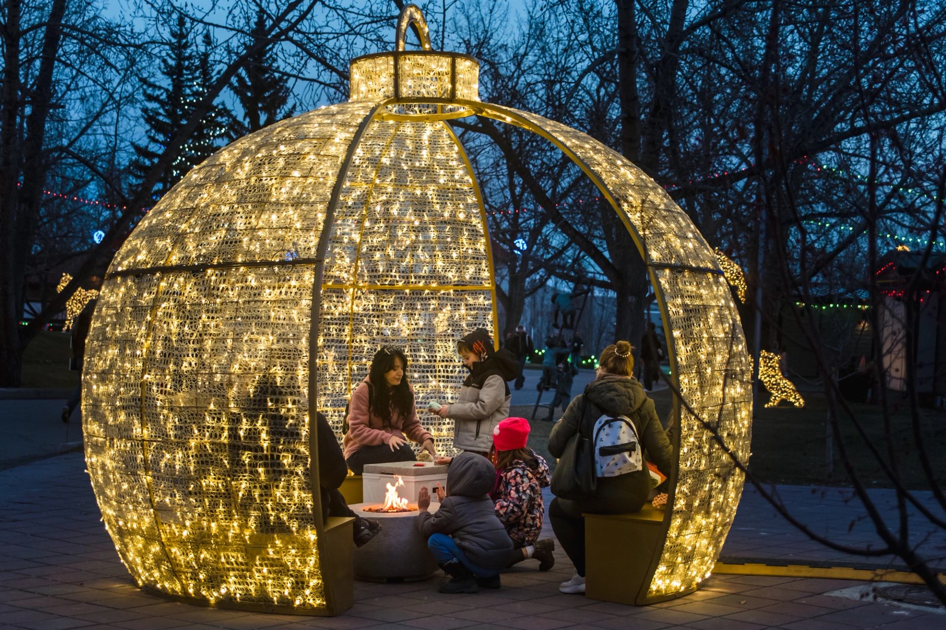 People sitting inside a large illuminated ornament sculpture around a small fire feature.