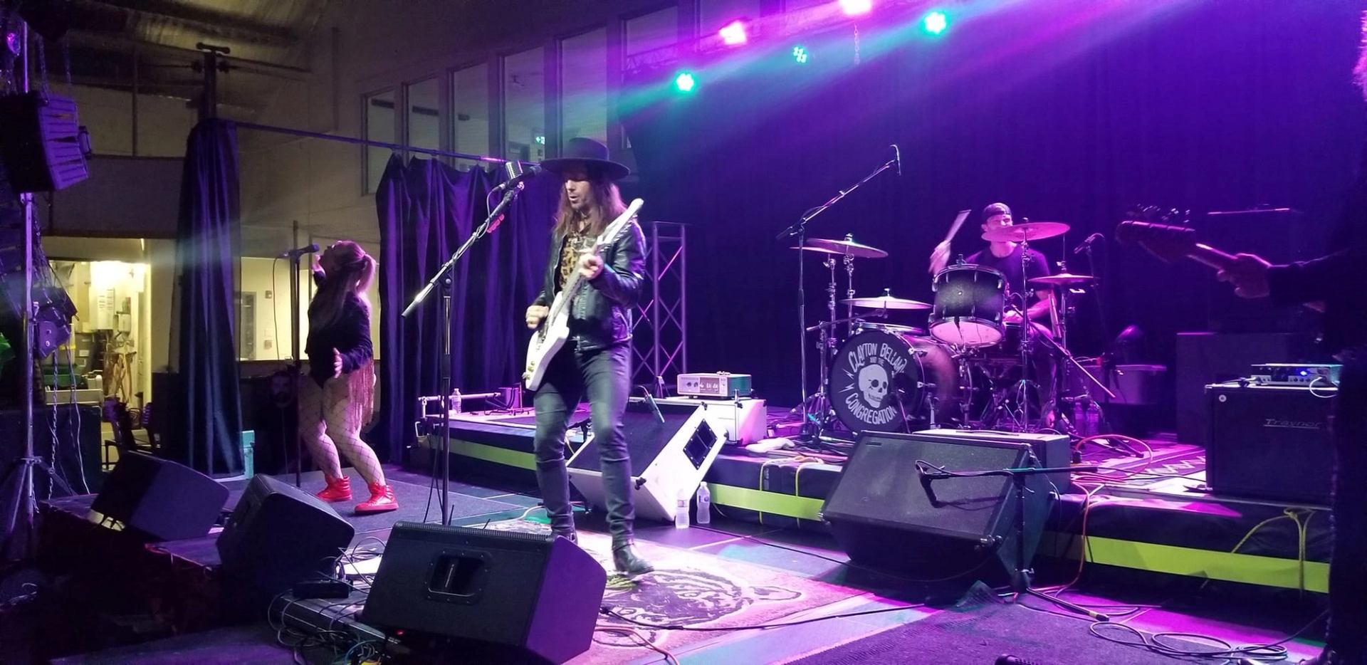 Guitarist and drummer perform under purple stage lights; drum reads Clayton Bellamy Congregation.