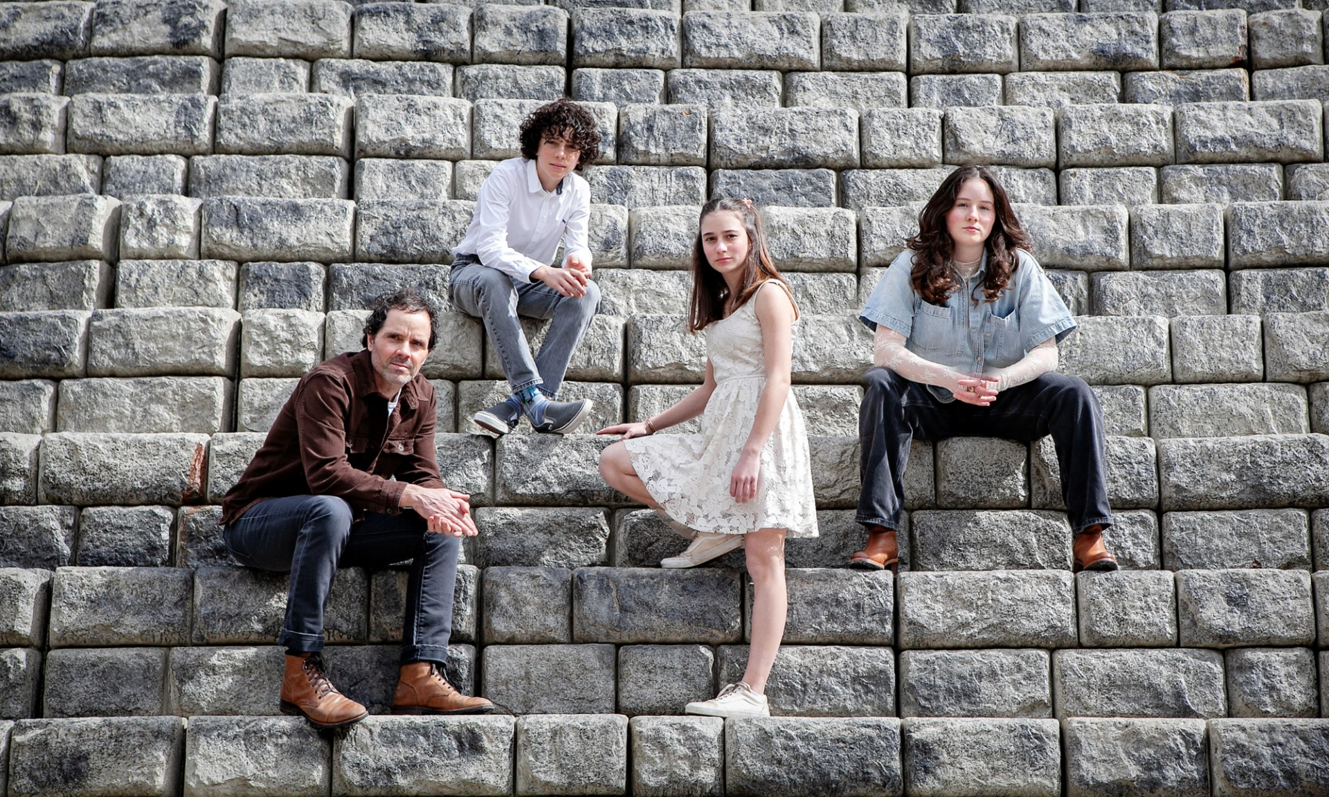 Four people sit on large stone steps, spaced apart, facing the camera.