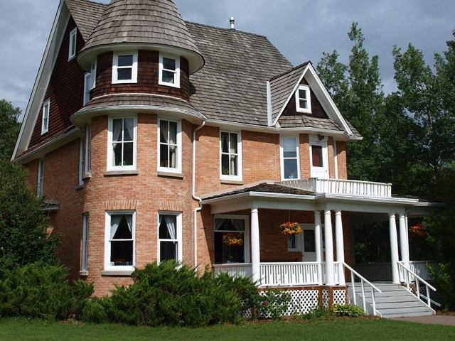 Historic red-brick Cronquist House with white trim and turret, surrounded by greenery.