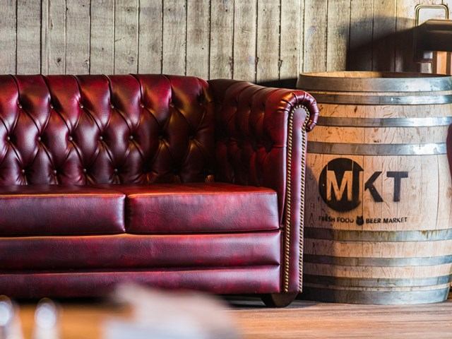 Red tufted leather sofa and MKT-branded barrel in a rustic wood-paneled room.