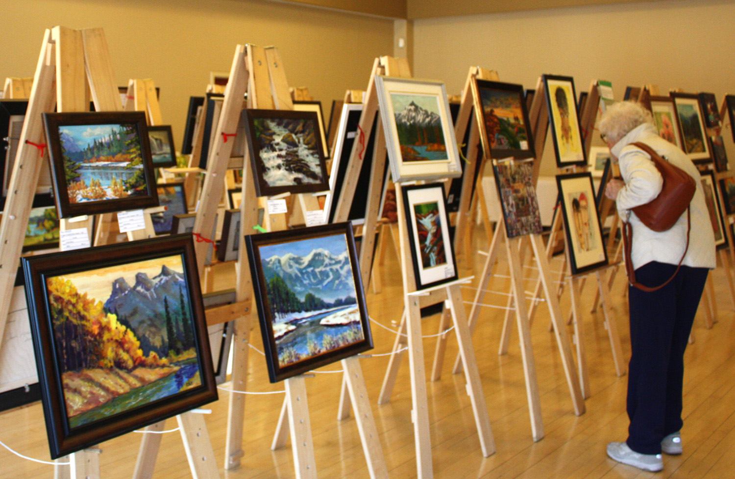 Art gallery with framed landscape paintings on wooden easels and a visitor viewing them.