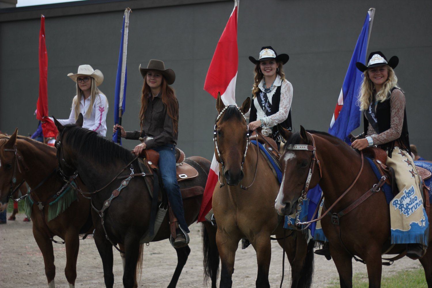 Riders in western clothing hold flags while sitting on decorated horses in an arena