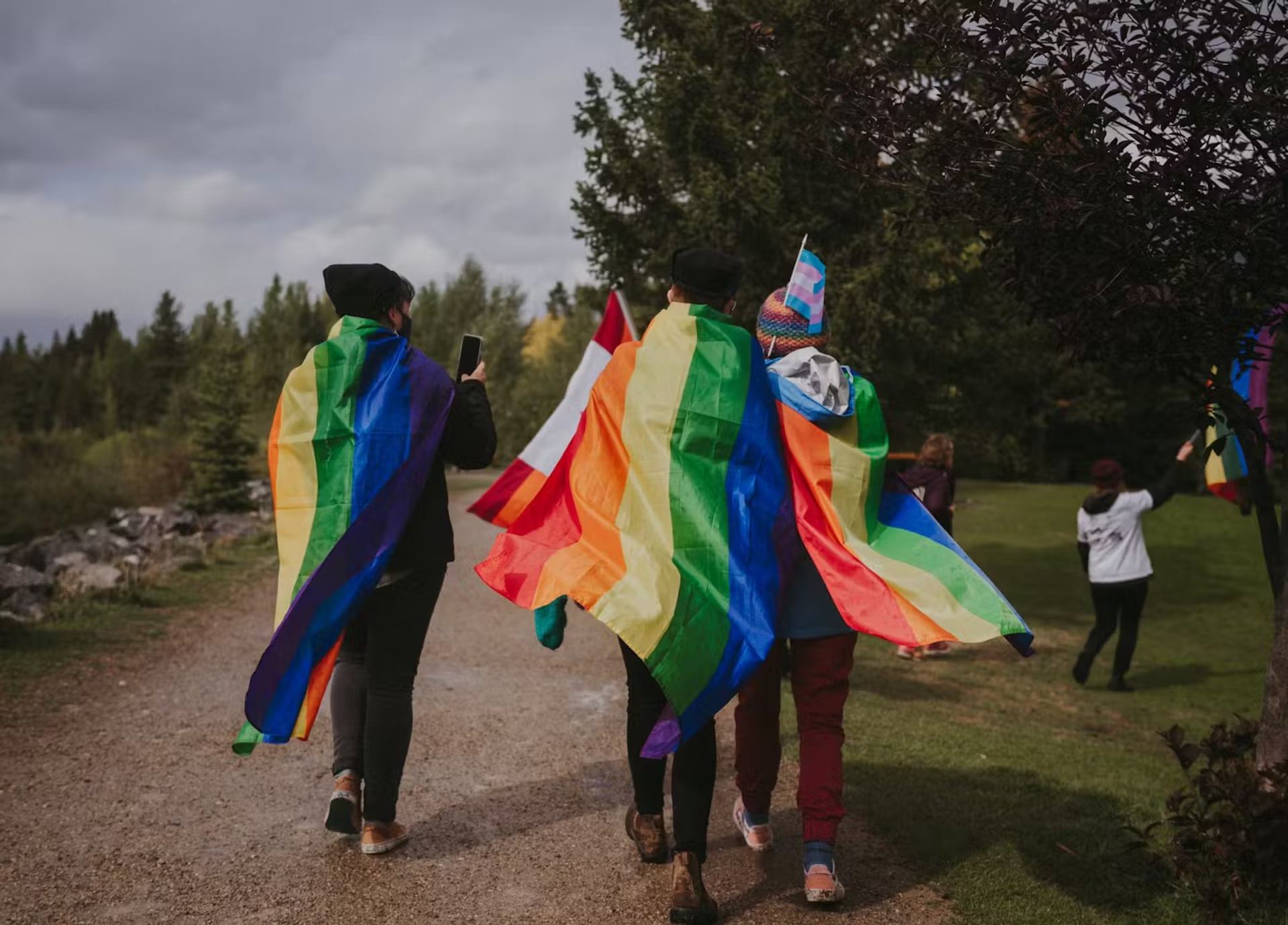 People walk outdoors draped in rainbow flags, celebrating LGBTQ+ pride.