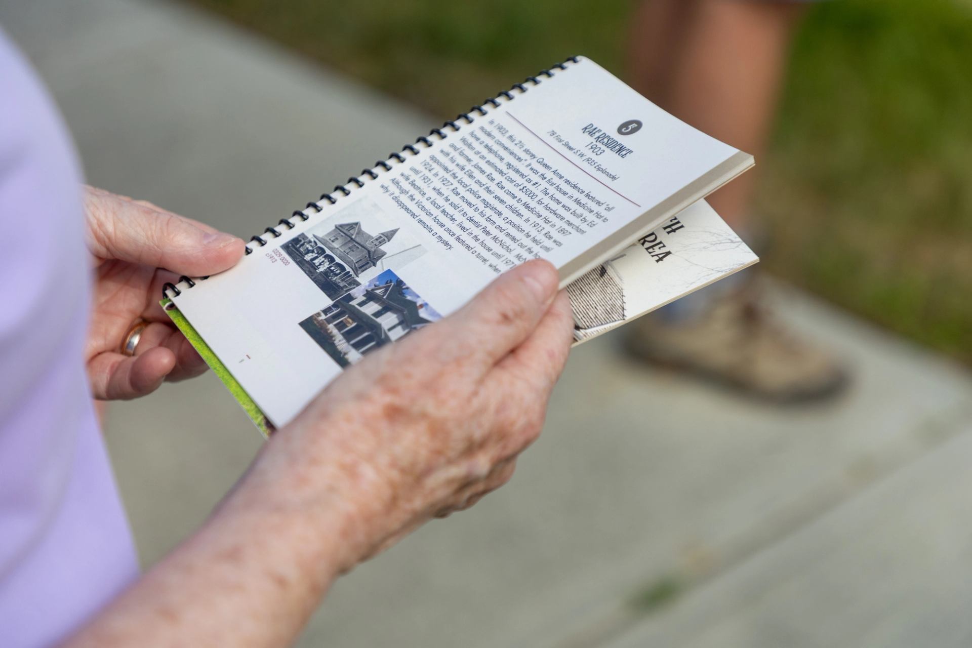Hands holding a spiral-bound booklet with historic house photos and text outdoors.