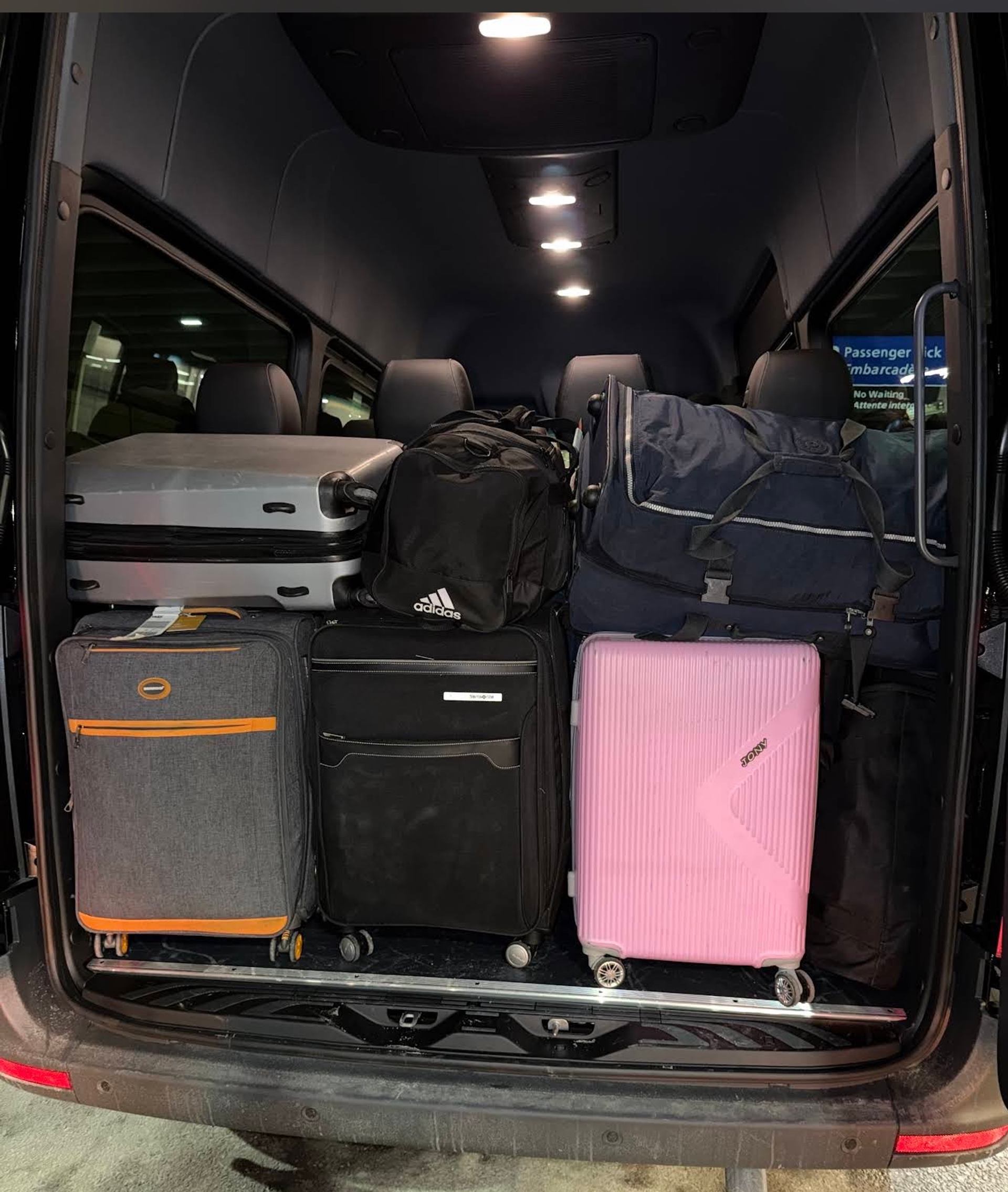 Open van trunk filled with assorted suitcases and bags under interior ceiling lights.