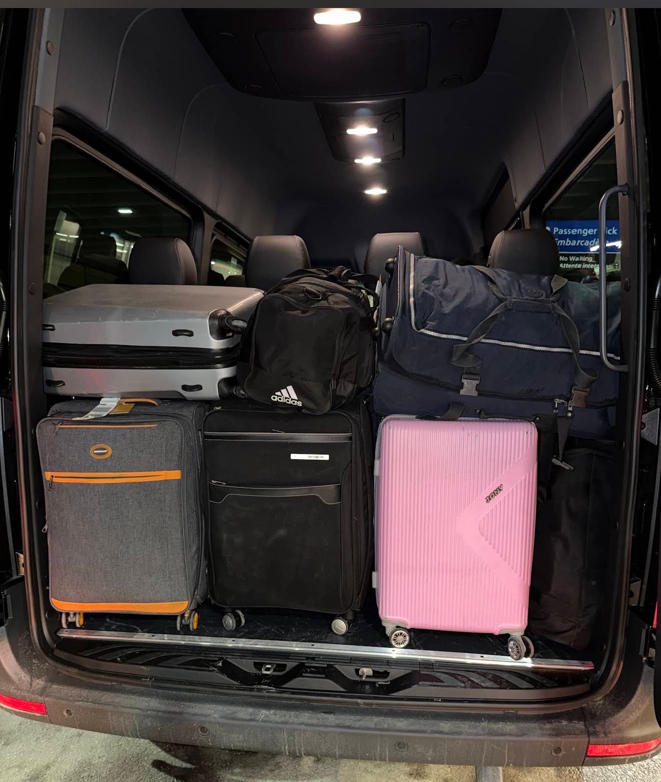 Open van trunk filled with assorted suitcases and bags under interior ceiling lights.