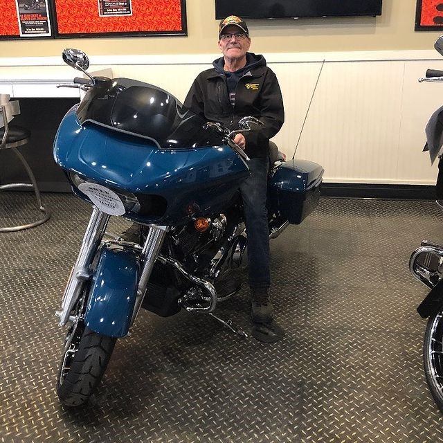 Person sitting on a blue touring motorcycle inside a showroom with framed posters.