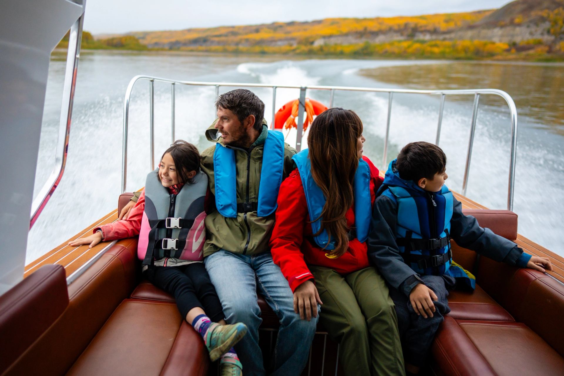 Family in life jackets boating past autumn trees on a scenic river.