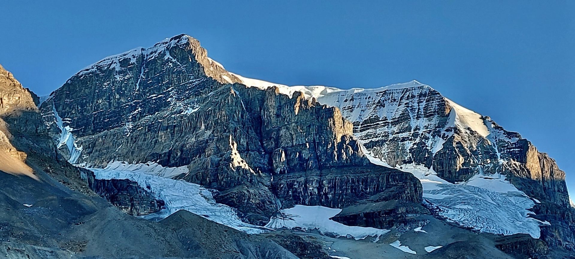 Rocky mountain peaks with layered cliffs, scattered snow patches and a descending glacier.