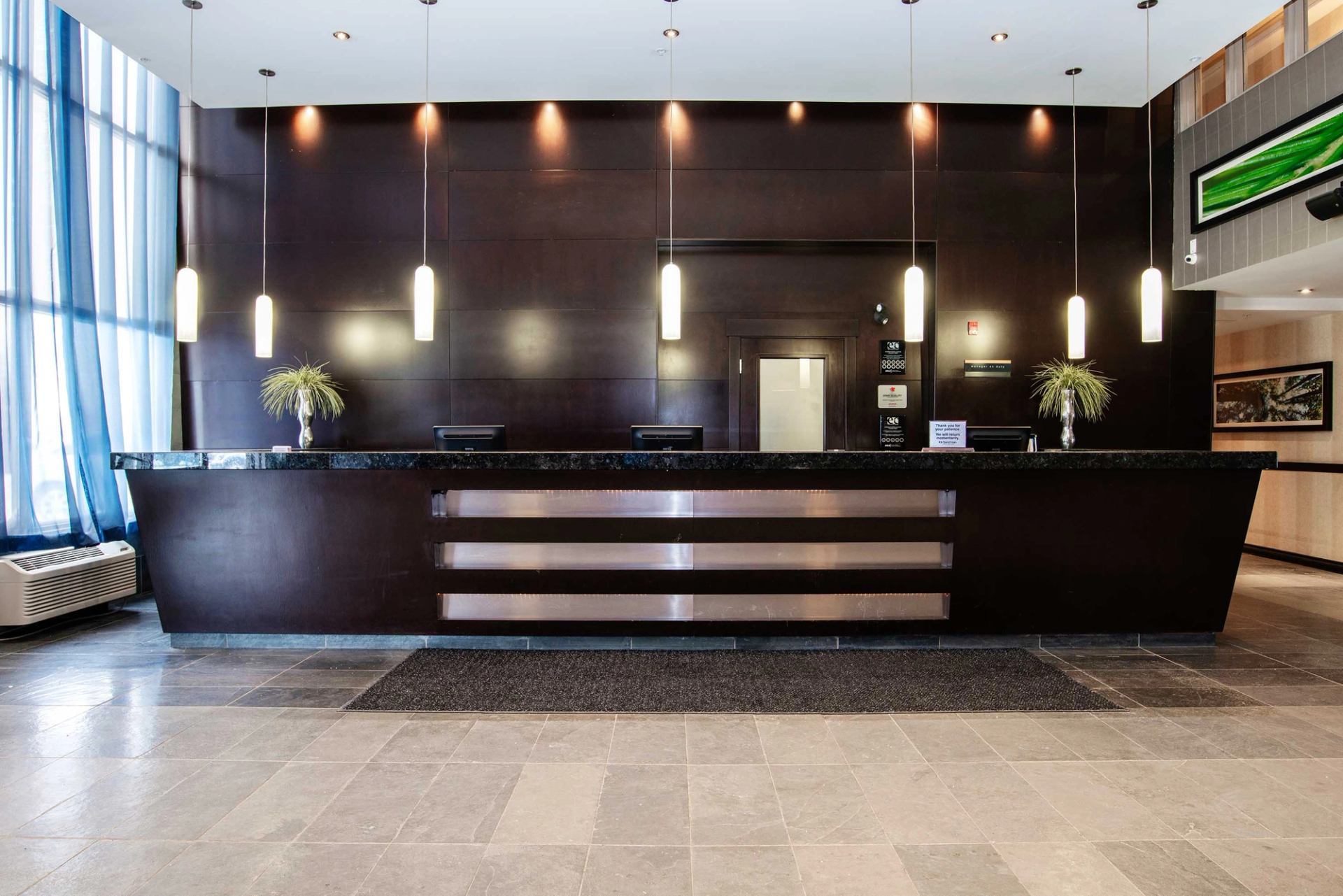 Hotel reception desk with pendant lights, dark wood panelling and potted plants.