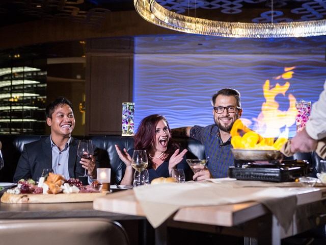 Diners at restaurant table with wine glasses and flame display in background.