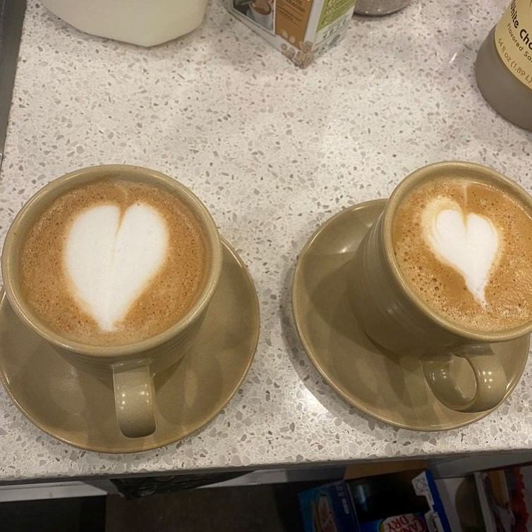 Two lattes with heart-shaped foam art on saucers, placed on a countertop.