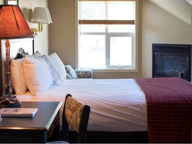 Cozy lodge room with fireplace, desk, armchair, and bed with red throw blanket.