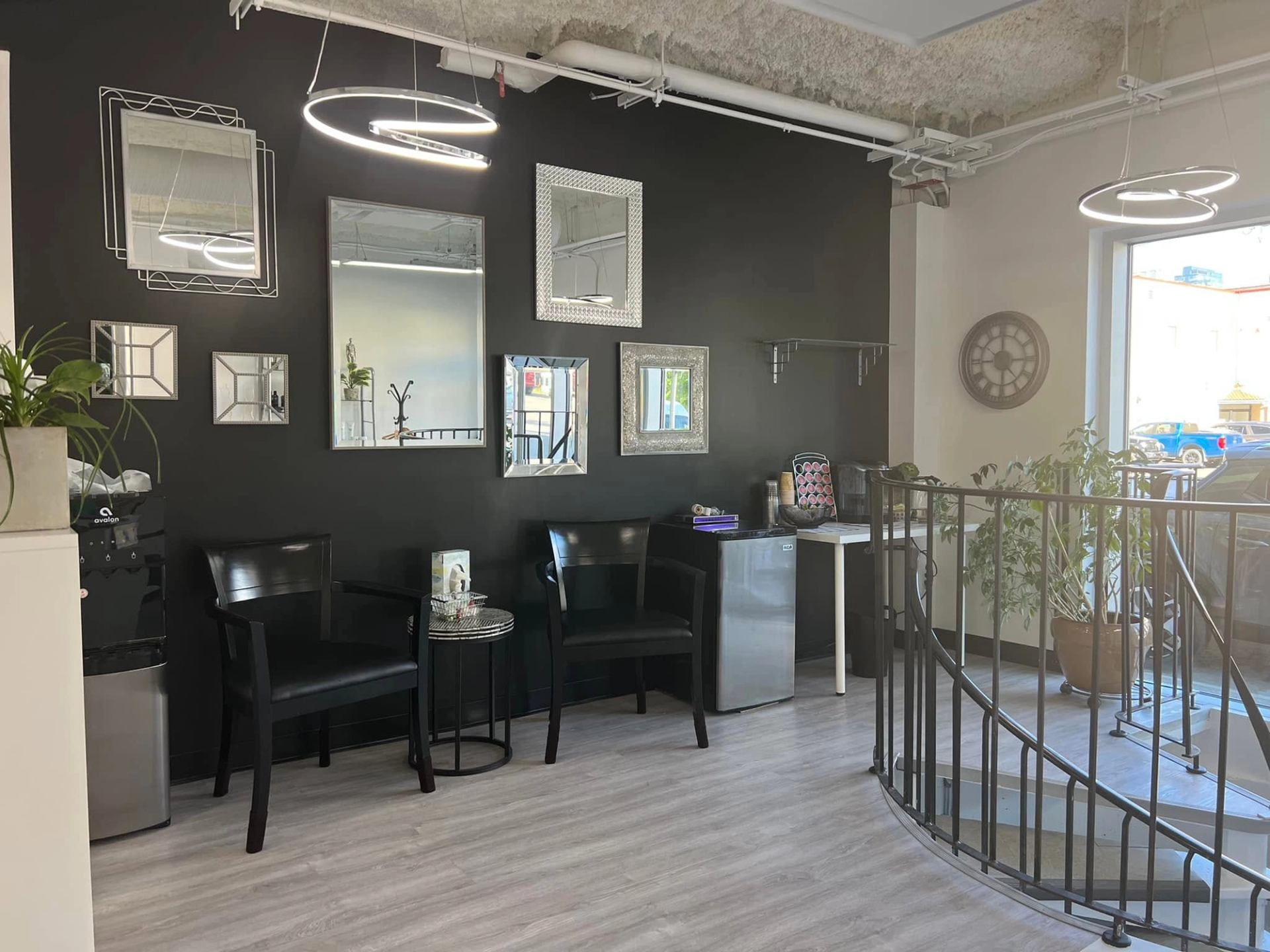 Modern waiting area with black chairs, wall mirrors, coffee station and spiral staircase.