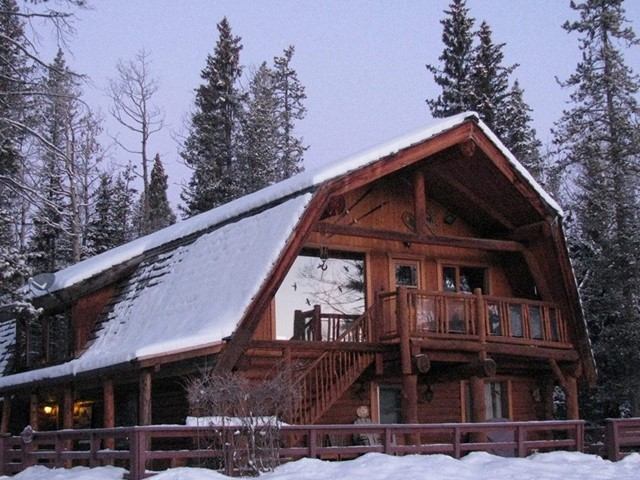 Snow-covered log cabin surrounded by tall pine trees at Folk Tree Lodge.