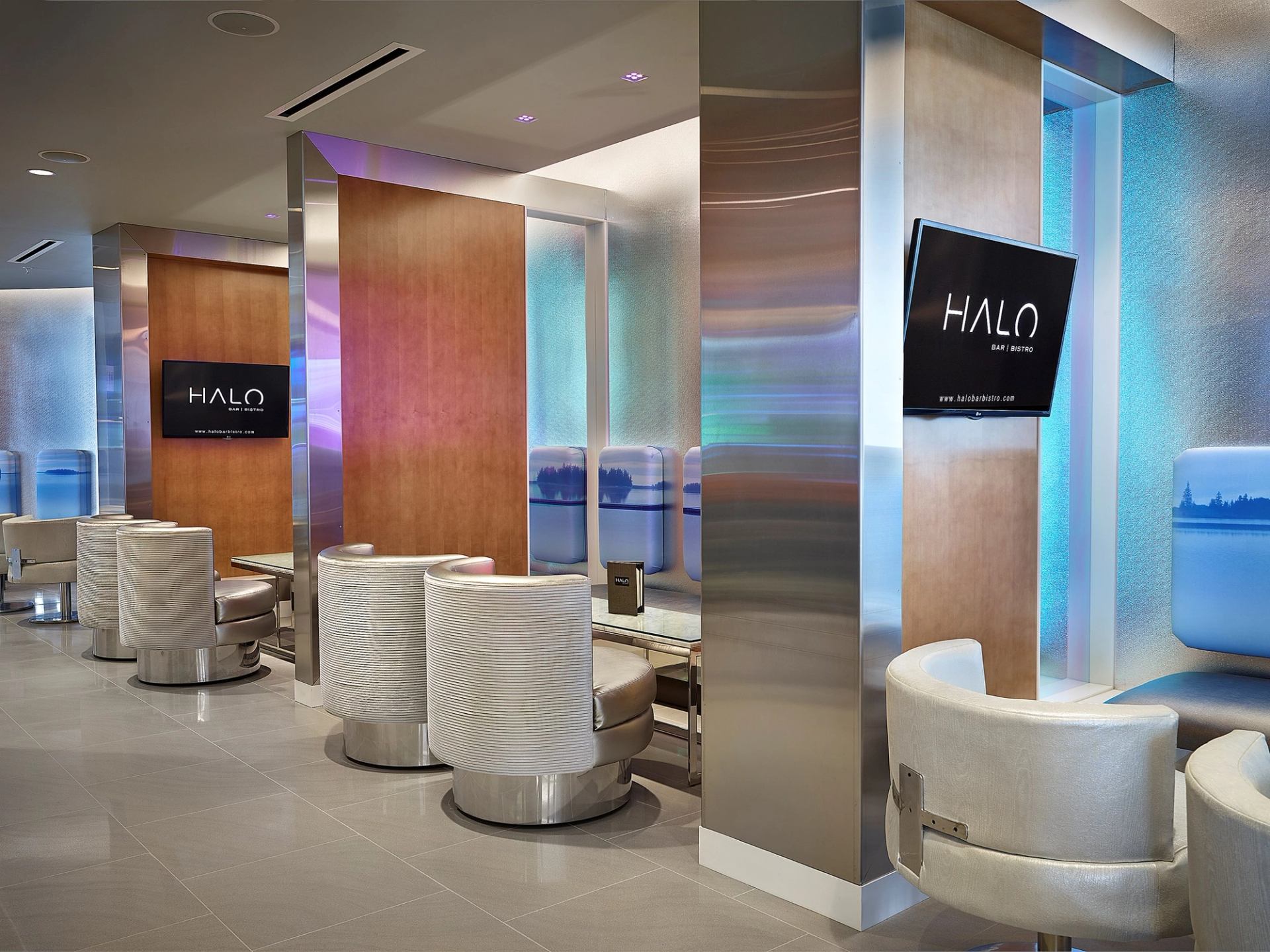 Upscale lounge booths with white chairs, wood panels, and ambient lighting at HALO Bar|Bistro.