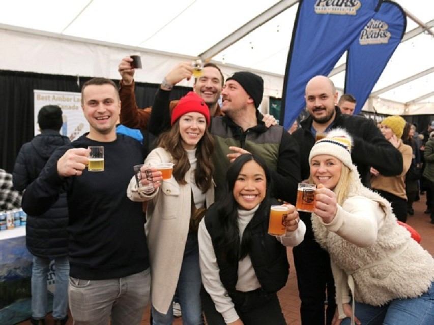 Group of friends smiling with drinks at indoor beer festival.