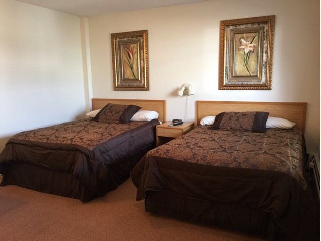 Two double beds with dark bedding and framed floral art in a simple hotel room.