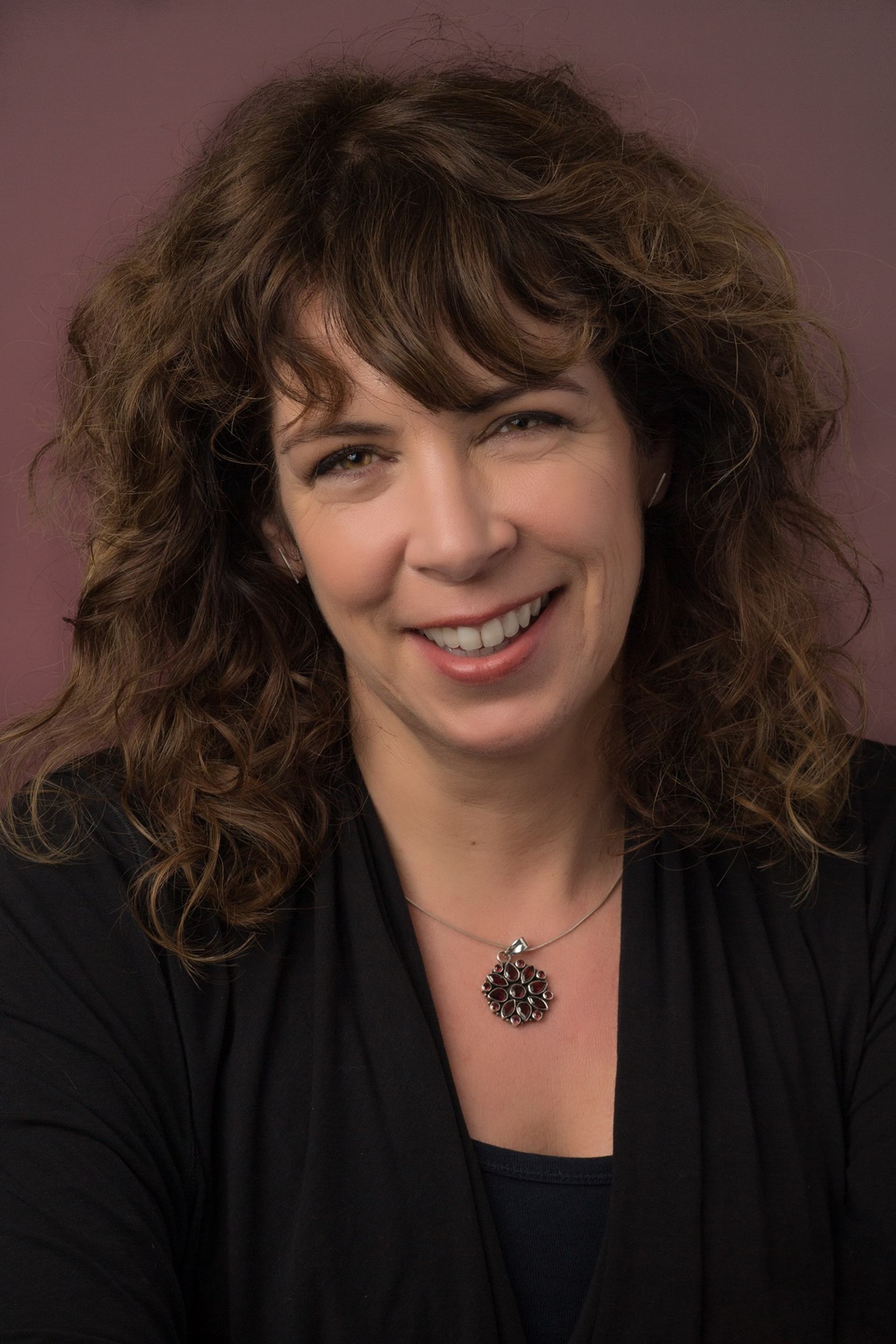 Portrait of Rhonda Mullins wearing a dark top and a decorative pendant.
