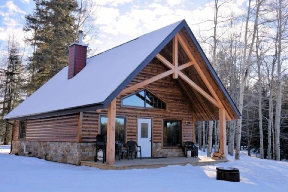 Snow-covered log cabin with porch seating in a winter forest setting.