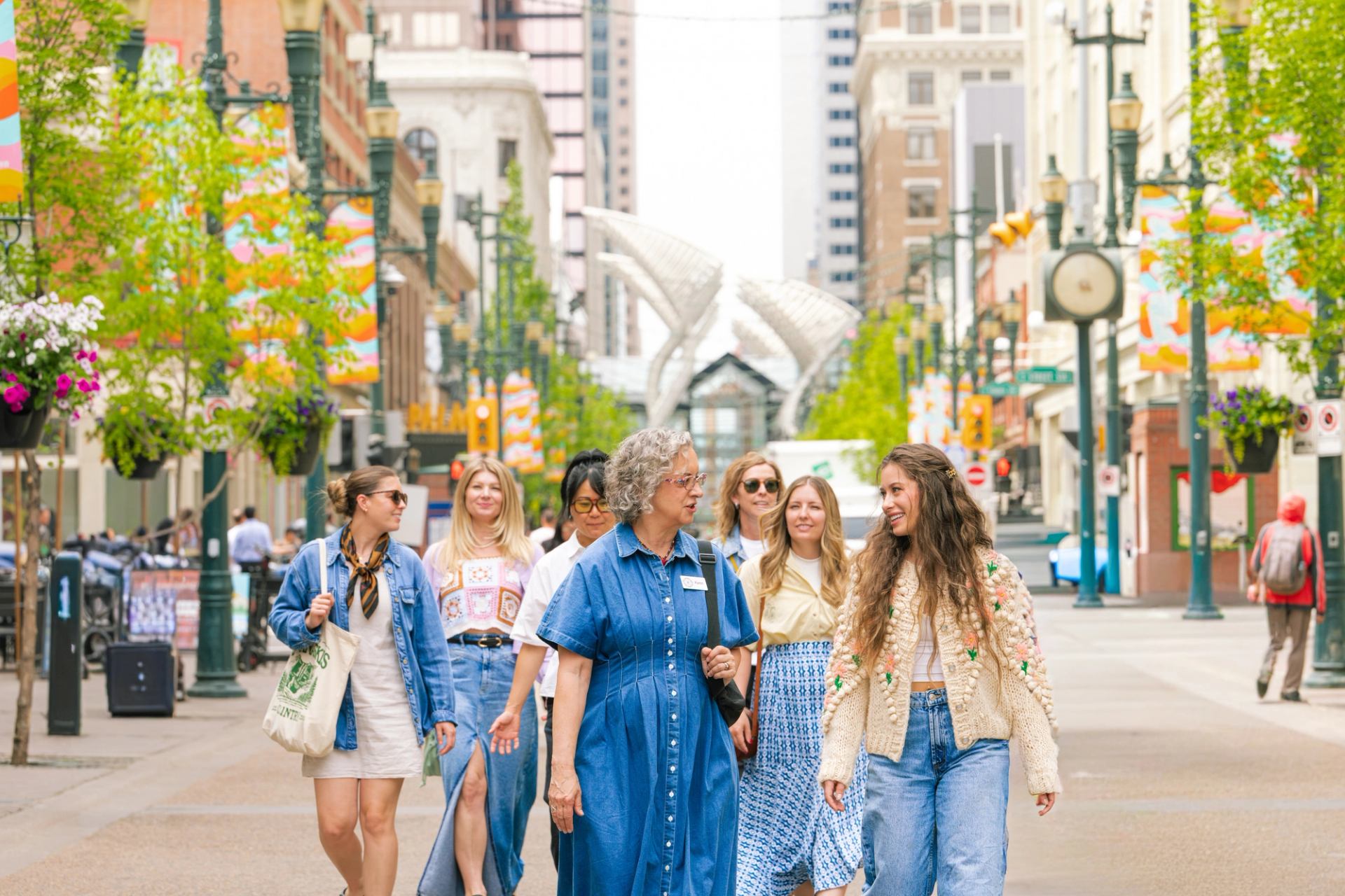 Group of people walking along a colourful downtown pedestrian street with banners and trees.