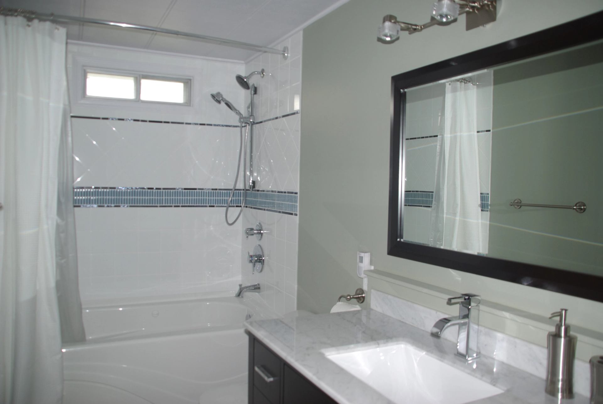 Bathroom with white tub, blue tile accent, and marble vanity with mirror