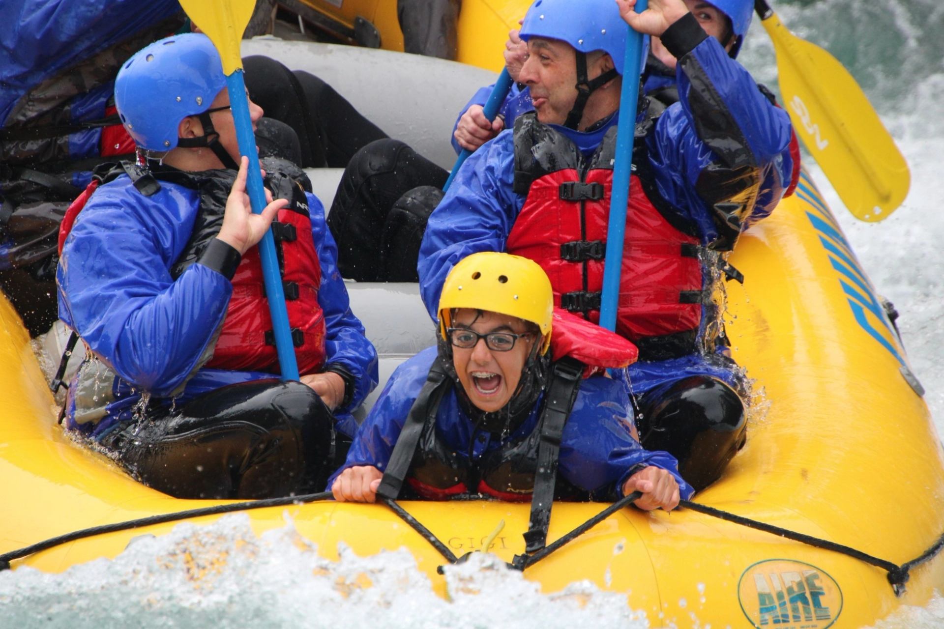 Group of people in helmets and lifejackets whitewater rafting in a yellow inflatable boat.