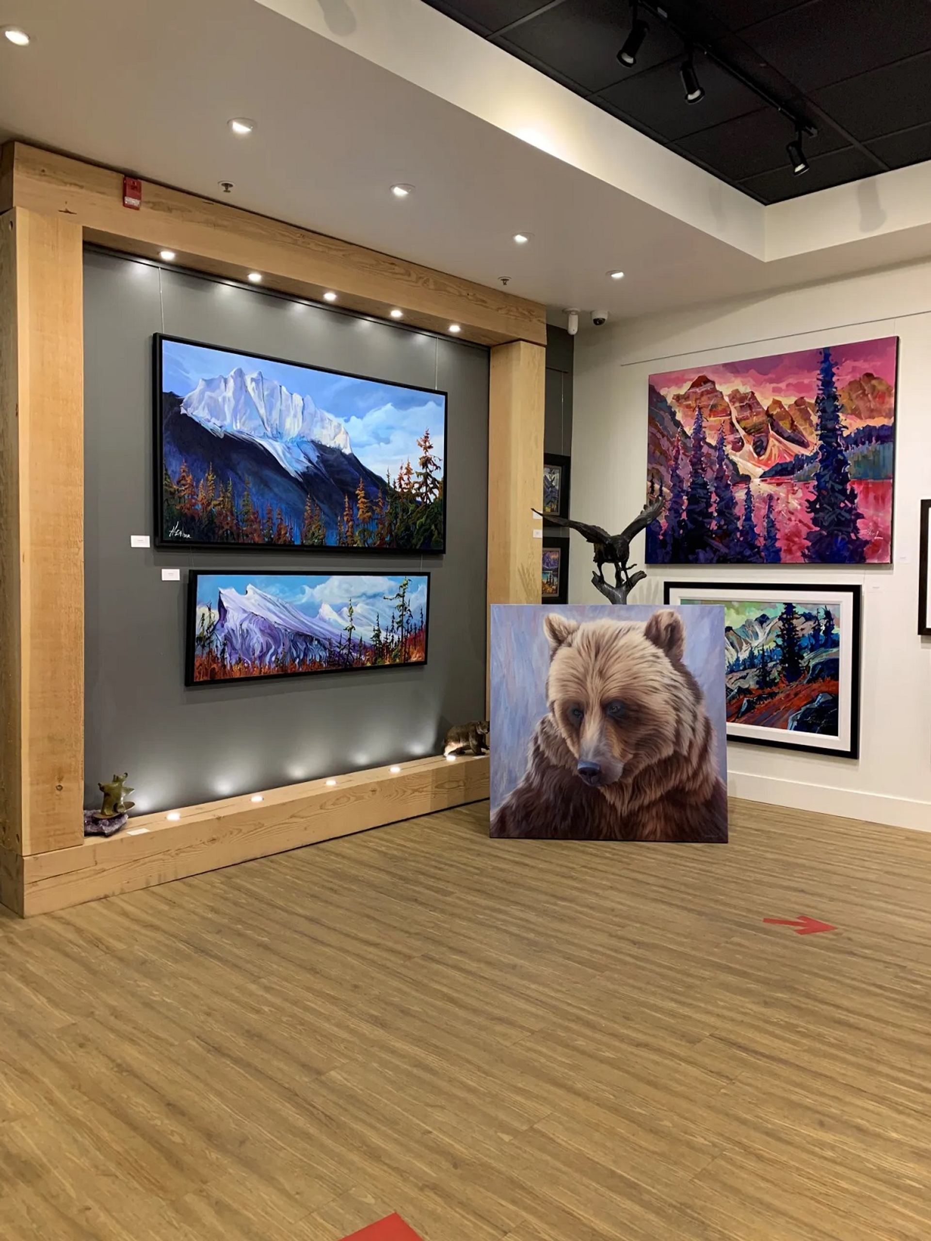 Art gallery featuring vibrant landscape paintings, a bear portrait, and a bird sculpture.