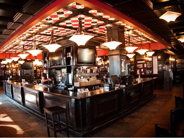Cozy bar interior with U-shaped counter and checkered ceiling.