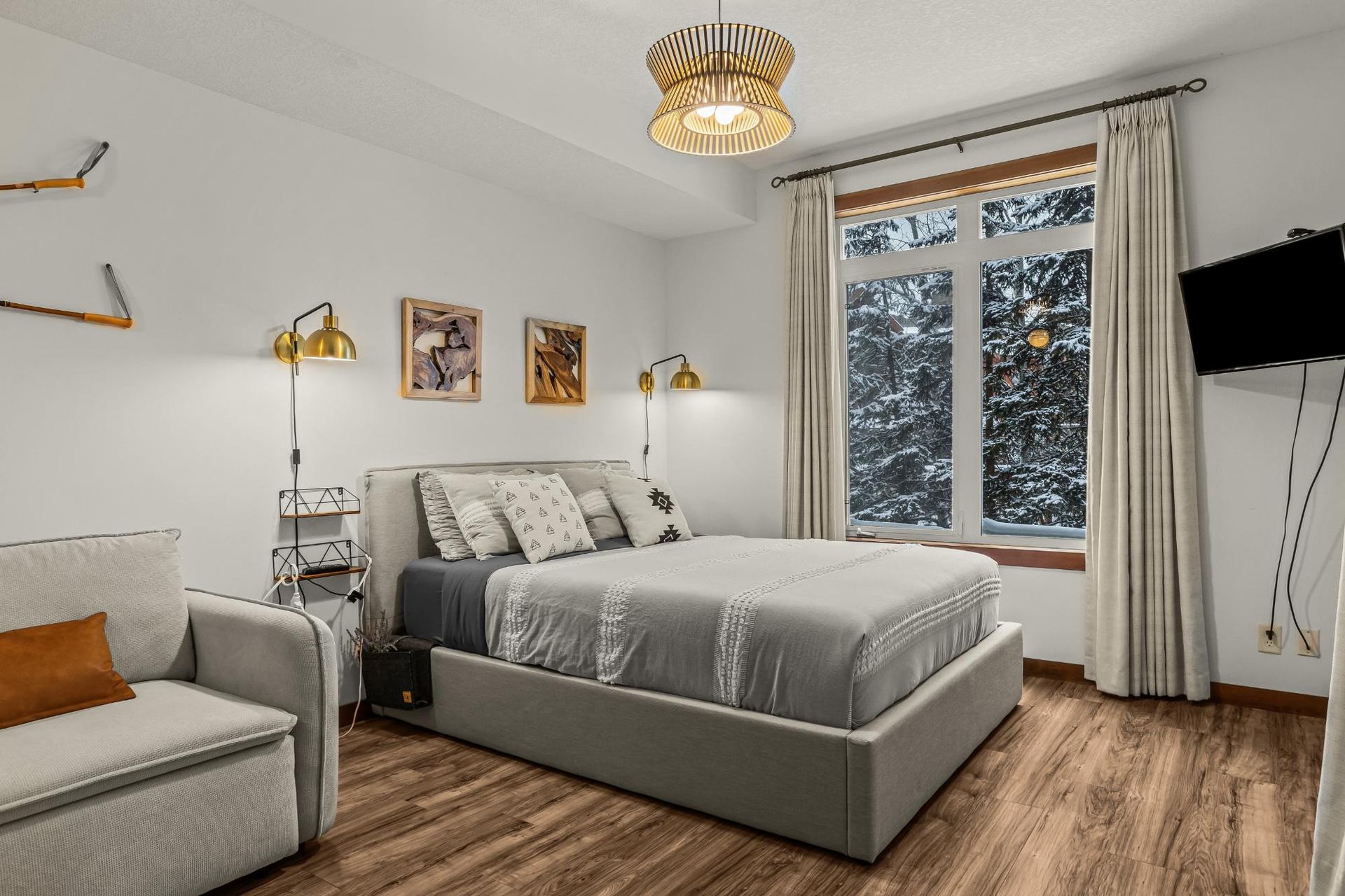 Bedroom with grey bed, sofa, wall art and snowy trees visible through window.