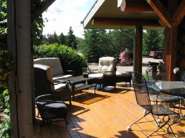 Cozy patio with cushioned seating, wooden beams, and lush garden backdrop.
