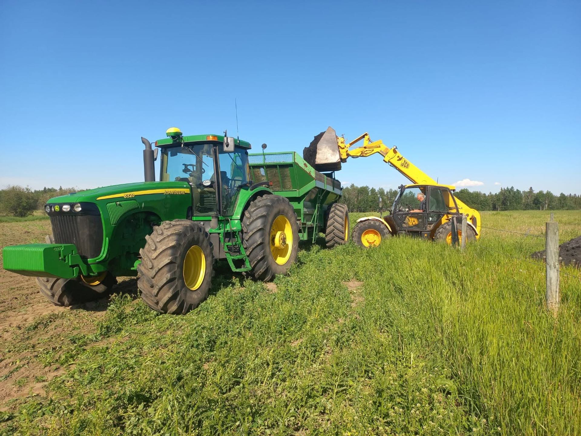 A tractor and loader move compost across a field under a clear blue summer sky.