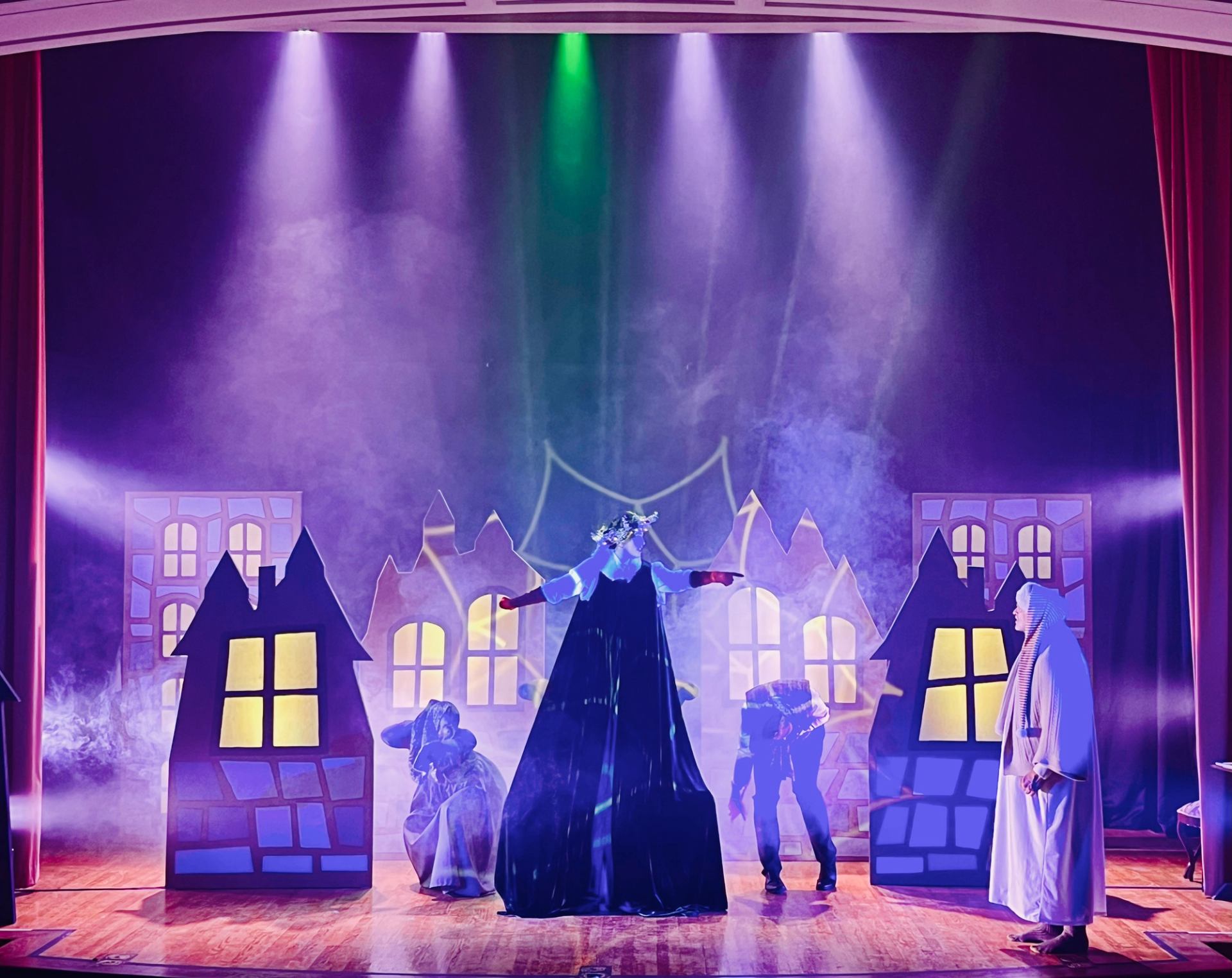 Actors perform with a colourful glowing village background.