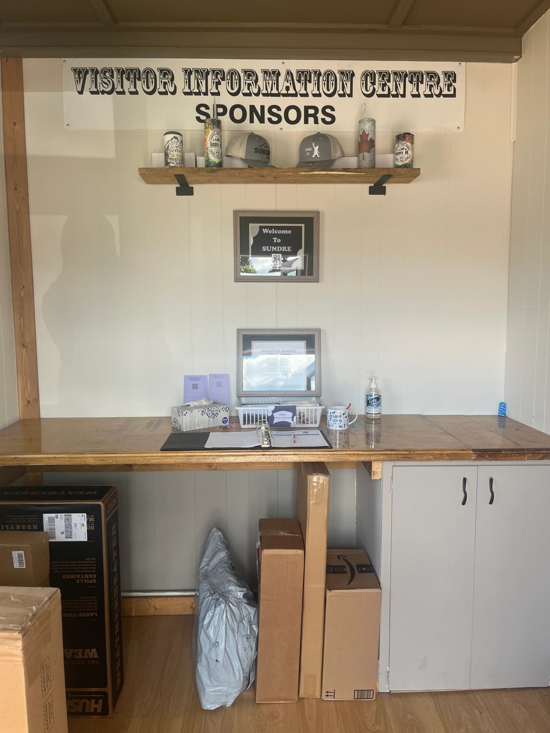 Sundre Visitor Centre display with sponsor hats, awards, and items on a wooden shelf.
