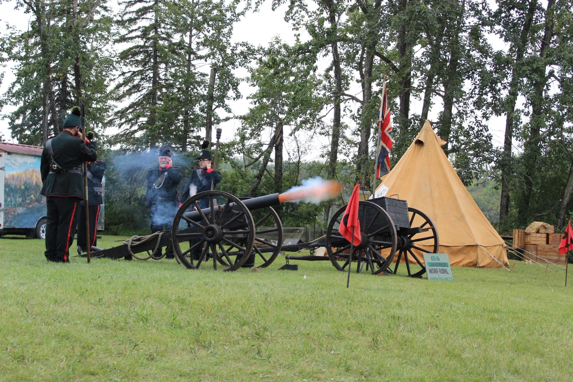 Costumed historical re-enactors fire a cannon beside a canvas tent and British flag.
