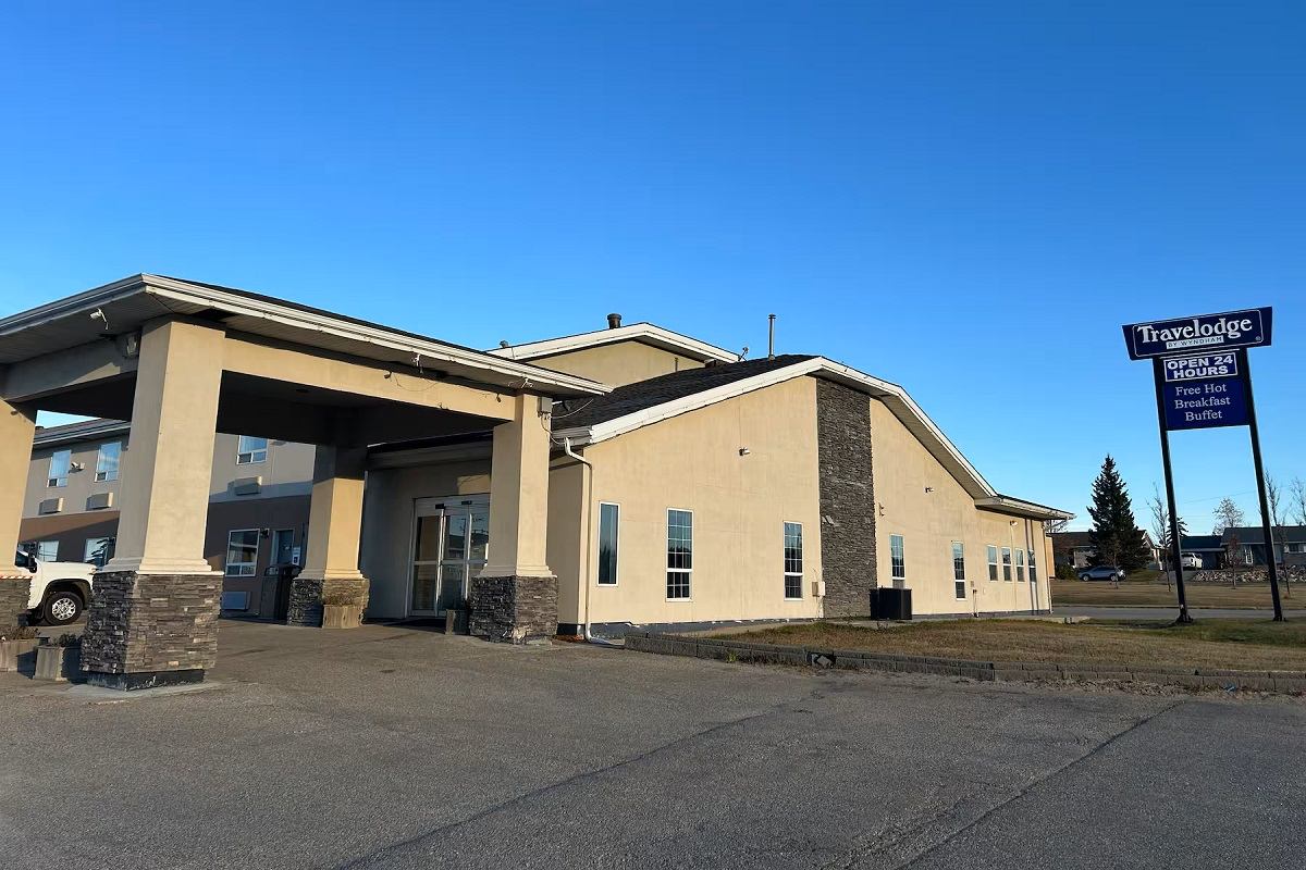 Exterior view of a cream-colored Travelodge hotel with a stone-accented entrance and a blue Travelodge sign.