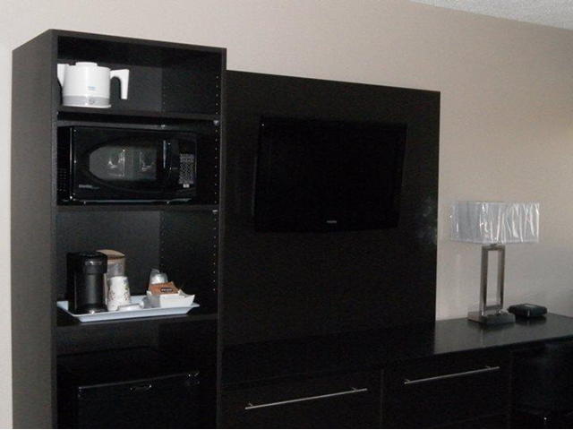 Microwave and coffee maker in black cabinet beside TV in hotel room.