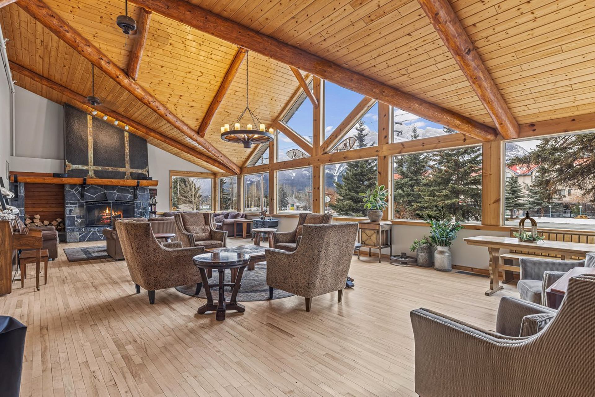 A cozy lodge lobby with a vaulted wood ceiling, large stone fireplace, comfortable armchairs, and windows revealing a mountain view.