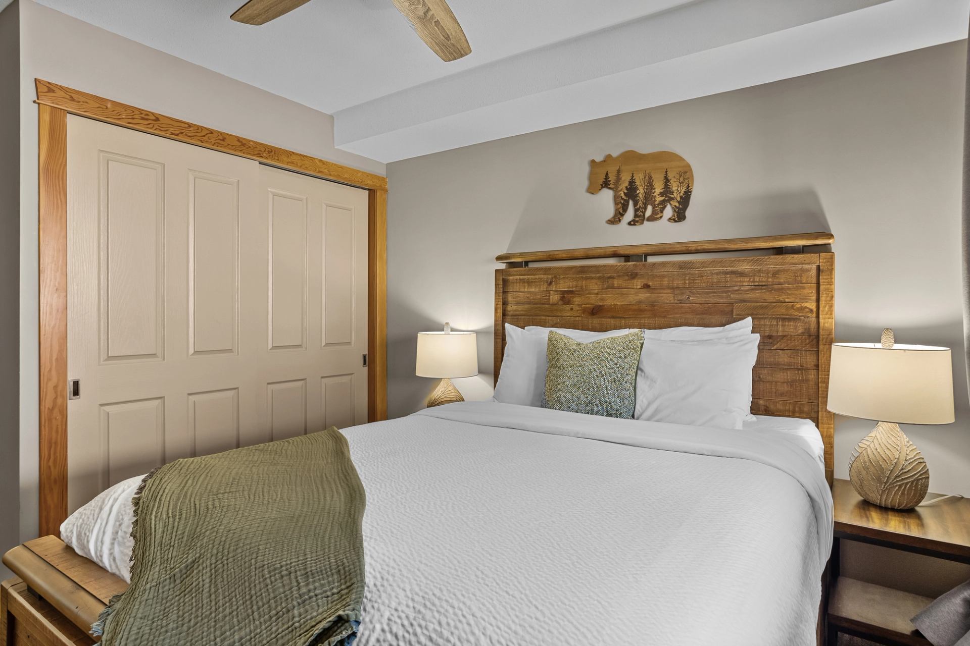 Bedroom with wooden bed frame, white bedding, two lamps, and bear wall art above the headboard.
