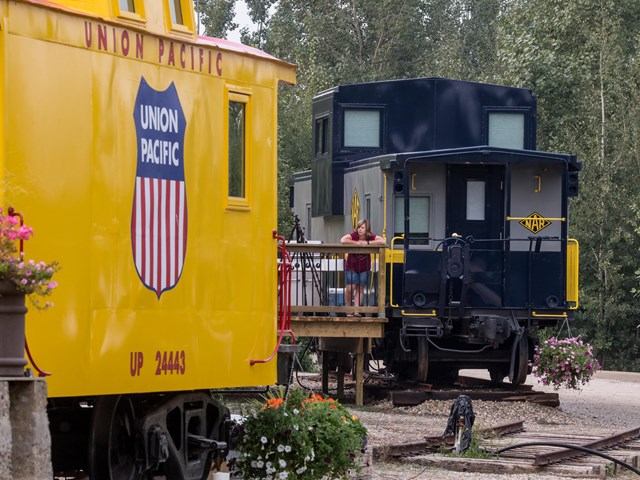 Two colorful train cabooses, one yellow Union Pacific, with a person standing on a wooden deck.