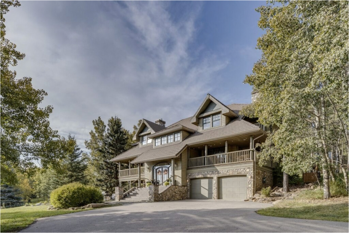 Large stone and wood house with balconies, double garage and tree-lined driveway.