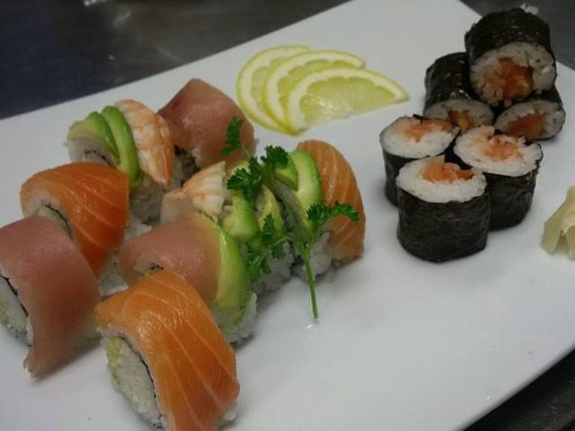 Plate of assorted sushi rolls with salmon, avocado, shrimp, and lemon garnish.